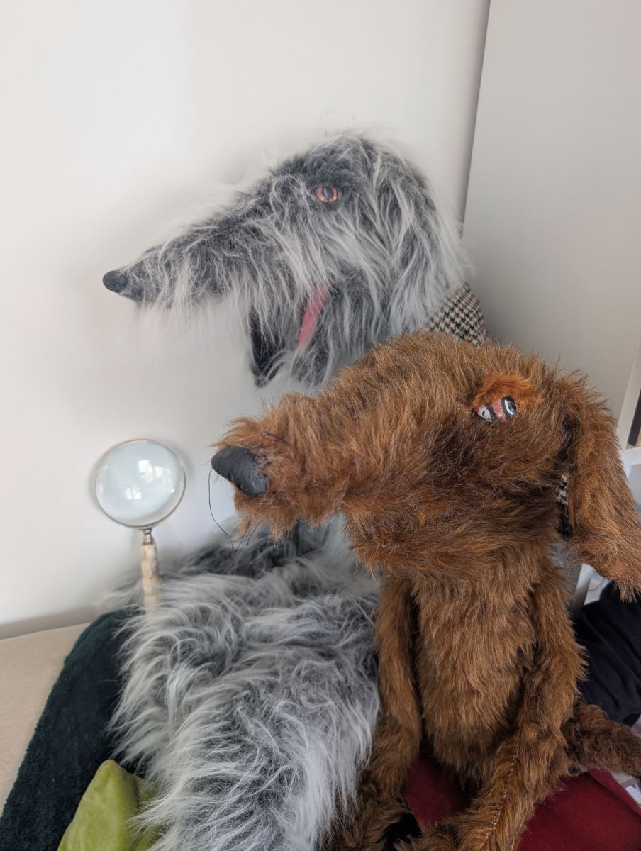 Puppets of a grey dog holding a magnifying glass and a brown dog looking to the left