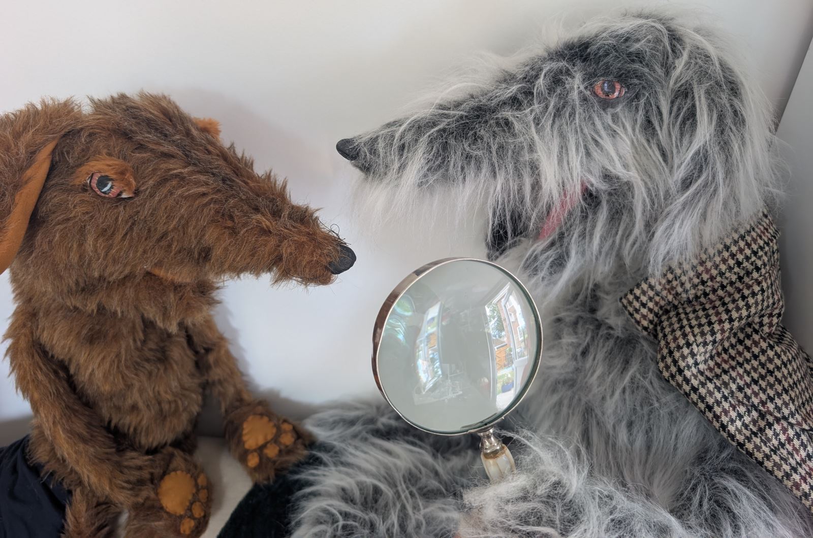 Puppets of a grey dog holding a magnifying glass and a brown dog looking at each other