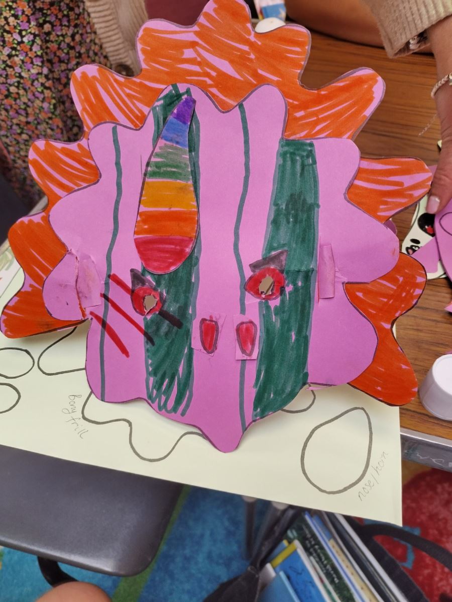 a pink and orange triceratops mask with a rainbow horn and red eyes and nose